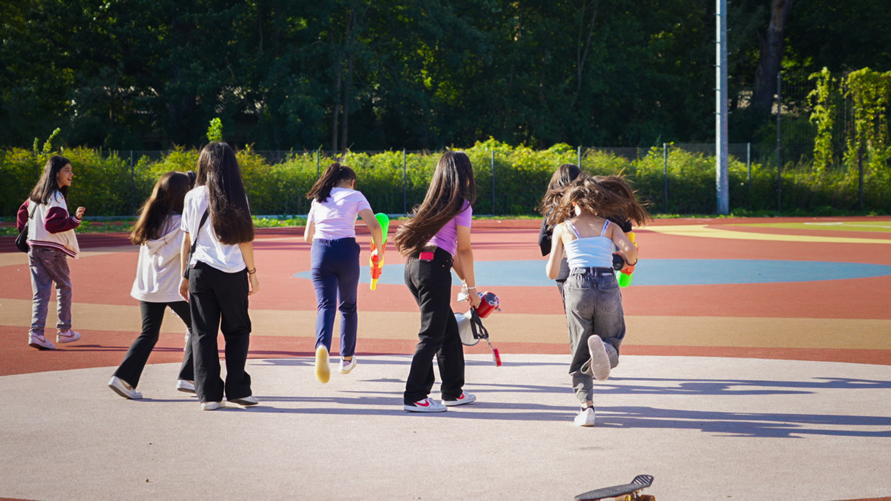 Sechs Jugendliche laufen über einen Sportplatz mit Wasserspritzpistolen in der Hand